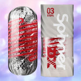 Two cylindrical objects are shown: on the left is a transparent spiral sleeve with a red pattern; on the right, a white case labeled "Tenga Spinner DX 03 Steps" from brand Tenga with red and black text.